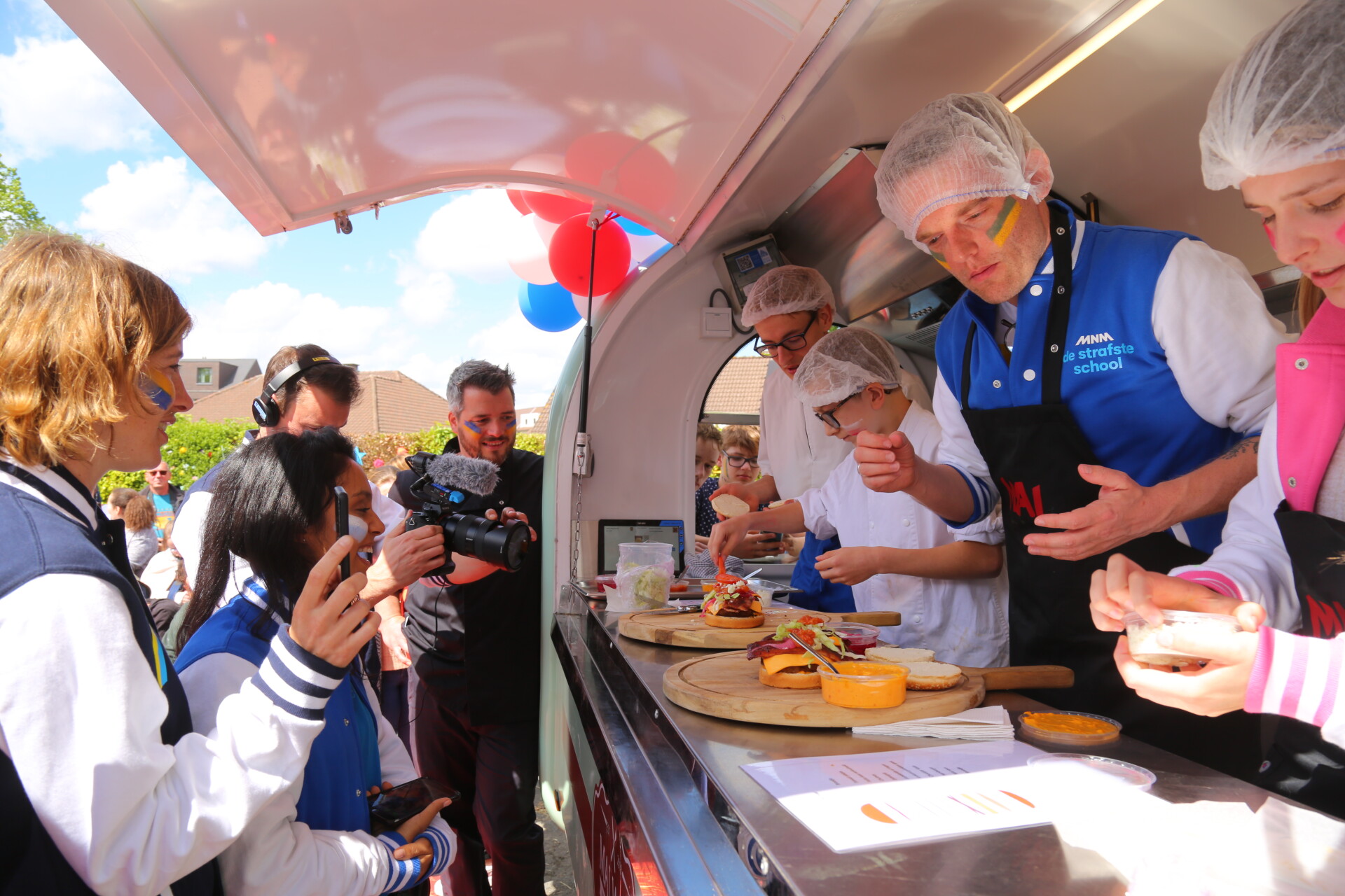 Tom De Cock neemt het op tegen leerlingen van het MAI in hamburgers bakken